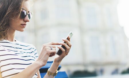 Hipster texting message on smartphone or technology, mockup of blank screen. Girl using cellphone on building castle background close. Tourist female hands holding gadget on blurred summer backdropの写真素材