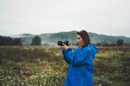 photographer tourist girl in blue raincoat shooting on photo camera froggy mountainの写真素材
