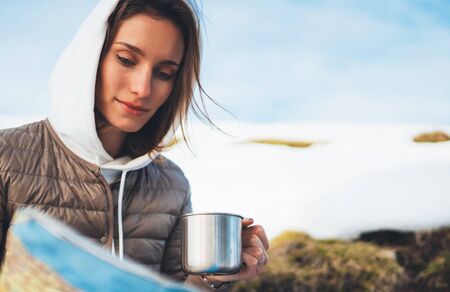 girl holding in hand cup of drinks, people planning trip in snow mountain, tourist look on map, hipster on background winter nature, enjoy journey landscape vacation trip, lifestyle holiday conceptの写真素材