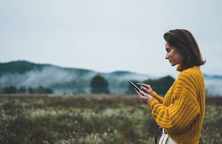 photographer girl hold in hands mobile phone typing message on smartphone on background autumn froggy mountain, internet online conceptの写真素材
