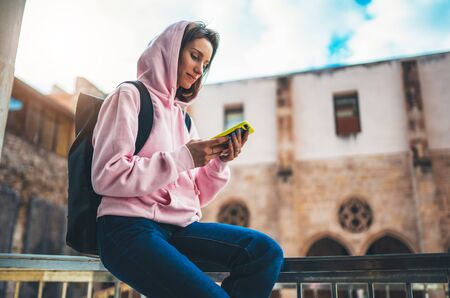 girl hold in hands mobile phone, person type message on smartphone in sun city, relax tourist travels planning trip, hipster enjoy journey in cityscape, lifestyle holiday concept, internet onlineの写真素材