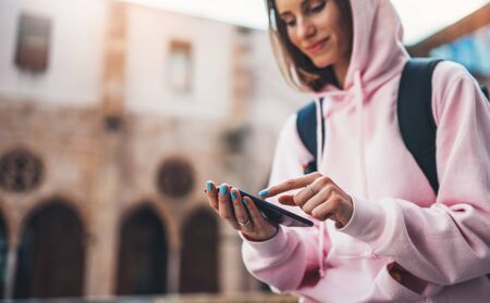 girl hold in hands mobile phone in sun city, person type message on smartphone, relax tourist travels planning trip, hipster enjoy journey in cityscape, lifestyle holiday concept, internet onlineの写真素材