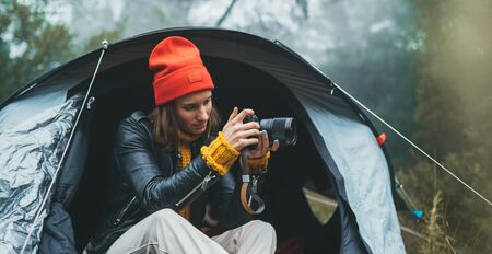 photographer tourist traveler take photo on camera in camp tent in froggy rain forest, hiker woman shooting mist nature trip, green trekking tourism, rest vacation concept camping holidayの写真素材