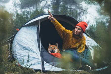 tourist traveler hugging red shiba inu in camp tent on background froggy rain forest, happy hiker woman with puppy dog in mist nature trip, friendship love concept, girl resting dog togetherの写真素材