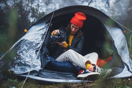 photographer tourist traveler take photo on camera in camp tent in froggy rain forest, hiker woman shooting mist nature trip, rest vacation concept camping holidayの写真素材