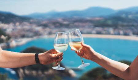 Drink two glasses white wine in friends hands outdoor sea nature holidays, romantic couple toast with alcohol, happy people cheering fun vacation enjoying travel time together friendship love concept congratulationsの写真素材