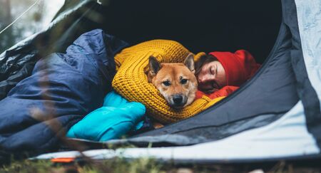 girl hug resting dog together in campsite, red shiba inu tourist sleeping in camp tent , hiker woman leisure with puppy dog relax nature vacation, friendship love conceptの写真素材