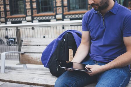Hipster texting message on tablet computer or technology screen mockup. Smile young man using digital on building castle background. Male hands tourist holding gadget on blur cityscapeの写真素材