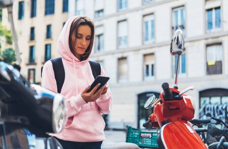 girl hold in hands mobile phone, person type message on smartphone, tourist traveler planning trip on moto scooter, hipster enjoy journey in cityscape, lifestyle holiday concept, internet onlineの写真素材