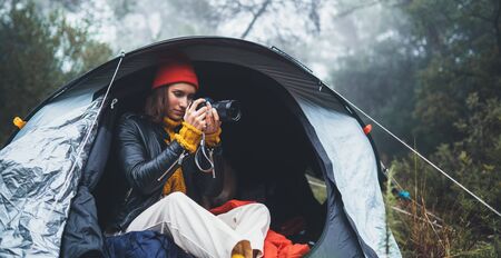 photographer tourist traveler take photo on camera in camp tent in froggy rain forest, hiker woman shooting mist nature trip, green trekking tourism, rest vacation concept camping holidayの写真素材