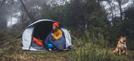 tourist traveler hugging relaxation red shiba inu in camp tent on background froggy forest, hiker woman with puppy dog in mist nature trip, friendship concept, copy spaceの写真素材