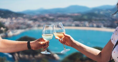 Drink two glasses white wine in friends hands outdoor blue sea nature holidays, romantic couple toast with alcohol, happy people cheering fun vacation enjoying travel time together friendship love concept congratulationsの写真素材