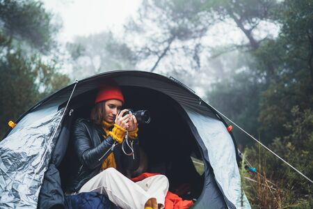 photographer tourist traveler take photo on camera in camp tent in froggy rain forest, hiker woman shooting mist nature trip, green trekking tourism, rest vacation concept camping holidayの写真素材