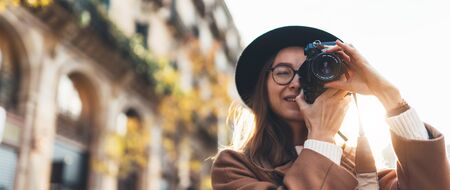 Photographer in glasses with retro photo camera. Tourist portrait girl in hat travels in Barcelona holiday. Sunlight flare street in europe city. Traveler hipster shoot architecture, copy space mockupの写真素材