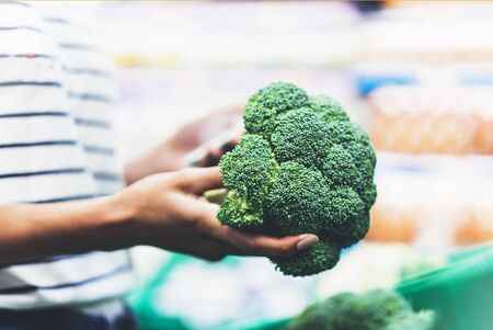 Young woman shopping healthy food in supermarket blur background. Female hands buy products broccoli using smartphone in store. Hipster at grocery using smartphone. Person comparing price of produceの写真素材