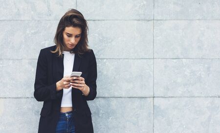 Portrait young businesswomen in black suit using smartphone isolated on background concrete gray wall mockup, pretty hipster manager holding mobile gadget, girl smiletexting message, connectの写真素材