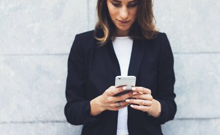 Portrait young businesswomen in black suit using smartphone isolated on background concrete gray wall mockup, pretty hipster manager holding mobile gadget, girl smiletexting message, connectの写真素材
