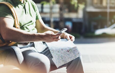Man with yellow backpack holding smartphone, tourist looking map city on background taxi, hipster planning route using in hands mobile phone, traveler connect wifi internet, backdrop summer street, mockupの写真素材