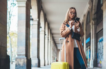 Tourist with suitcase holding smart mobile phone. Girl travels in Barcelona. Holiday concept in Spain street. Traveler hipster using cellphone online internet technology in europe trip. Copy space mockupの写真素材