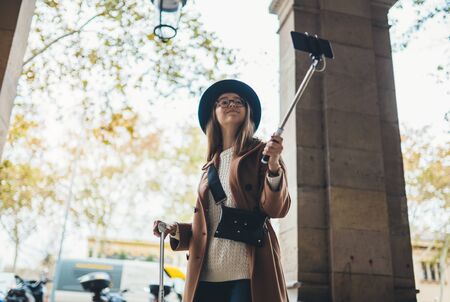 Tourist girl taking photo selfie on smartphone mobile. Blogger hipster travels in Barcelona. Holiday concept in Spain street. Traveler in glasses and hat self cellphone internet technology in tripの写真素材