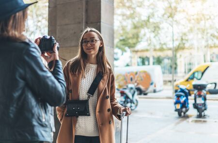 Photographer take photo model girlfriend. Blogger photoshoot concept. Tourist smiling girl in glasses travels in Barcelona holiday with traveler friend. Sunlight flare street in europe city copy spaceの写真素材