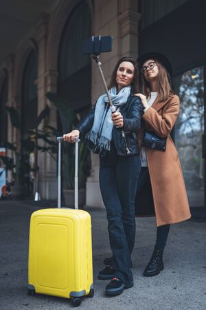 Girlfriends tourist with suitcase taking photo selfie together on smartphone mobile. Blogger hipster travels in europe city. Vacation holiday friendship concept. Travelers self cellphone internet technologyの写真素材