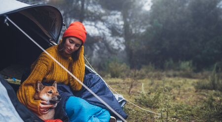 tourist traveler hugging relaxation red shiba inu in camp tent on background foggy forest, hiker woman with puppy dog in mist nature trip, friendship love concept, copy spaceの写真素材