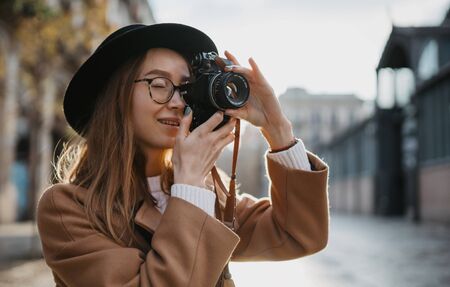 Photographer take photo on retro camera. Tourist portrait. Girl in hat travels in Barcelona holiday. Sunlight flare street in europe city. Traveler hipster shooting architecture, copy space mockupの写真素材