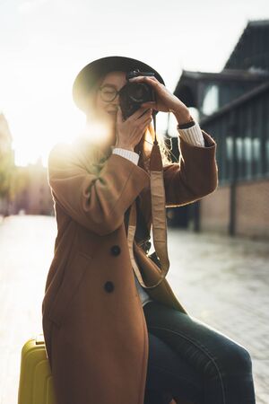 Photographer in glasses with retro photo camera. Tourist portrait. Girl in hat travels in Barcelona holiday. Sunlight flare street in europe city. Traveler hipster shooting architecture, copy space mockupの写真素材