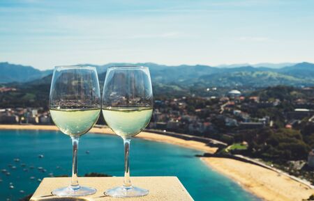 Two drink glass white wine standing on background blue sea top view city coast yacht from observation deck, romantic toast with alcohol panoramic cityscape downtown, spain san sebastian vacationの写真素材