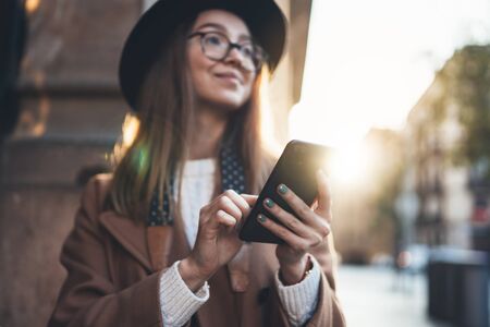 Woman holding in hands mobile phone crop. Close up technology smartphone online communication. Girl traveler in hat using gadget cellphone in europe sunlight city. Digital internet lifestyle mockupの写真素材