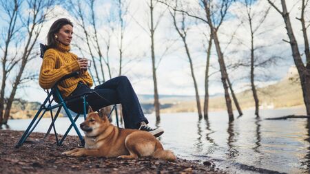 tourist traveler girl relax drink tea together dog on background foggy mountain, puppy pet hiker woman rest on lake shore nature tripの写真素材