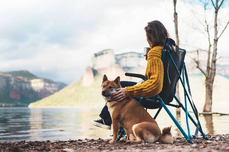 tourist traveler girl relax drink tea together friends dog on background mountain landscape,  woman hugging pet rest on lake shore nature tripの写真素材