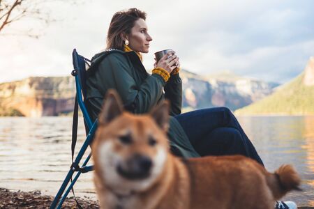 tourist traveler drink tea girl relax together dog on background mountain landscape,  woman hugging pet rest on lake shore nature tripの写真素材