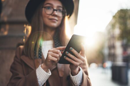 Traveler woman holding in hands mobile phone. Close up technology smartphone online connect. Girl hipster in glasses using gadget cellphone in europe sun flare city. Digital internet lifestyle mockupの写真素材