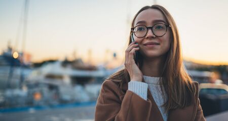 Traveler woman calling mobile phone in evening sea port Barcelona. Girl tourist in glasses using smartphone technology online gadget cellphone. Digital communicationの写真素材