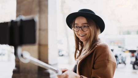 Tourist girl taking photo selfie on smartphone mobile. Girl hipster travels in Barcelona. Holiday concept in Spain street. Traveler smile in glasses and hat self cellphone internet technology in europe tripの写真素材
