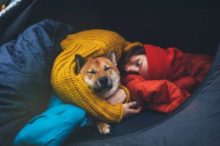 sleeping girl hug resting dog together in campsite, close up portrait red shiba inu leisure in camp tent , hiker woman with puppy dog relax nature vacation, friendship love conceptの写真素材