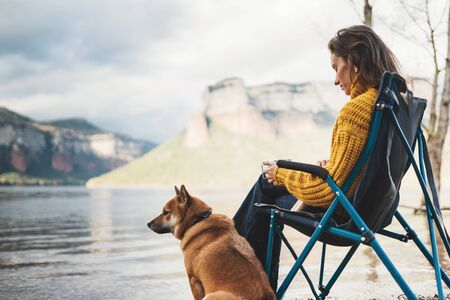 tourist traveler drink tea girl relax together dog mountain landscape,  woman hug pet rest on lake shore nature tripの写真素材