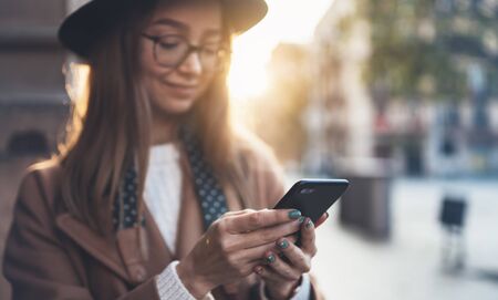 Traveler woman holding in hands mobile phone. Close up technology smartphone online. Girl tourist using gadget cellphone in sun flare city. Digital internet lifestyle communicationの写真素材