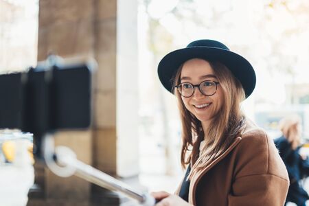 Tourist girl blogger taking photo selfie on smartphone mobile. Girl hipster travels in Barcelona. Holiday concept in Spain street. Traveler smile in glasses and hat self cellphone in europeの写真素材