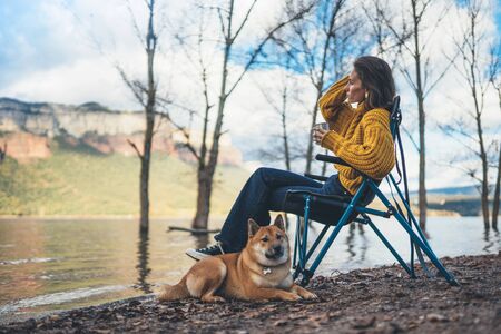 tourist traveler girl relax drink tea together dog on background mountain, puppy pet woman rest on lake shore nature trip, friendship conceptの写真素材