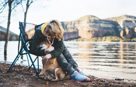tourist traveler girl together dog on mountain lake, happy woman hugging puppy pet nature,...