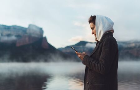 hipster tourist using smartphone planning trip on foggy lake, mist in mountain nature, traveler girl...