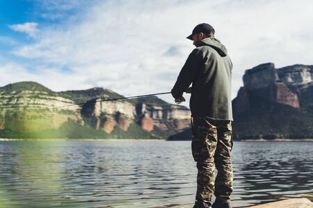 fisherman enjoy hobby with fishing rod on river, beard person catch fish on background mountain,...