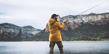 fishery concept, beard fisherman fishing rod, man enjoy hobby sport on lake, person catch fish on river on background mount, holiday relaxation vacation の写真素材