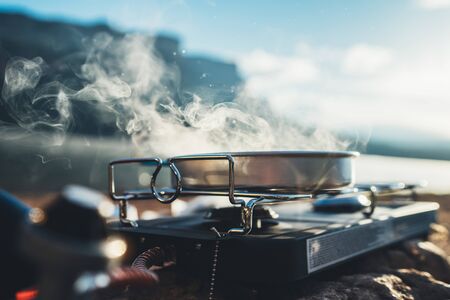 camping cooking in nature outdoor, prepare breakfast picnic in mist morning; vapours metal gas stove on stone; tourism recreation outside; campsite lifestyle, hot food hiking tripの写真素材