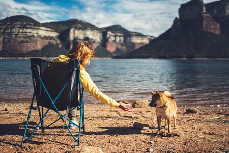 happy tourist traveler sits on lake, girl hiker enjoying mountains with pet dog, breathing of fresh air in trip in spain, relax holiday, journey leisure weekend の写真素材
