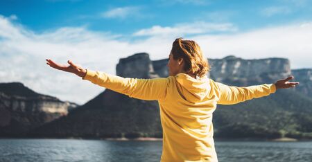 happy tourist traveler stand with raised hands, girl hiker enjoying mountains lake with arms outstretched breathing of fresh clean air in trip in spain, relax holidayの写真素材
