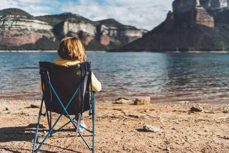 happy tourist traveler sits on lake, girl hiker enjoying mountains, breathing of fresh clean air in trip in spain, relax holidayの写真素材
